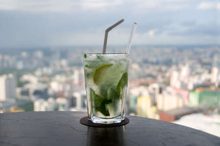 Mojito cocktail on rooftop bar with modern cityscape on the background. Singapore
