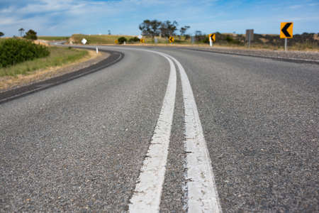 Close up of asphalt road in Australian countryside. Rural infrastructure landscape with winding road and yellow road signsの写真素材