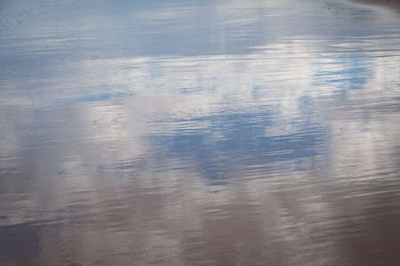 Blue sky and clouds reflected off wet sand on a beach. Water surface with sky reflection summer...