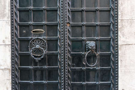 Closed old metal door with cast iron lattice and metal door handles, knockers