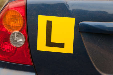 Yellow learner license plates on a back of dusty blue car. Learning to drive in a countrysideの写真素材