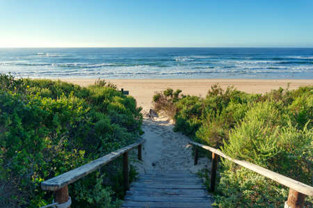 Ocean view beach background with wooden path covered in sand. Summer tropical beach vacation scene,...