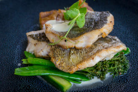 Close up of grilled fish fillets with broccolini florets and green peas and creamy sauce. For...