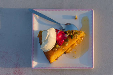 Top view of slice of sweet cake with cream and pistachio nuts and rose petal on a plate 