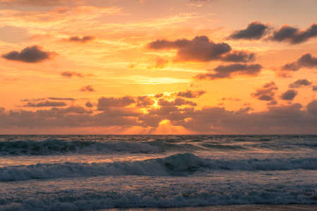 Beautiful sunrise seascape with colorful golden orange clouds and soft waves. Summer holiday nature...