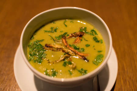 White plate with yellow peas cream soup garnished with green herbsの写真素材