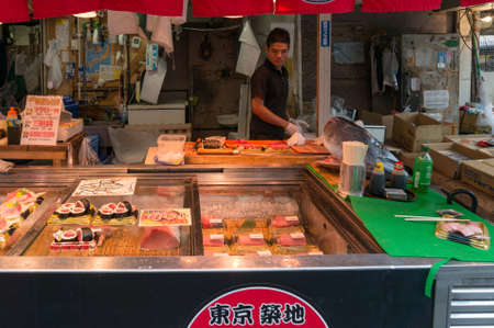 Tokyo, Japan - August 30, 2016: Fresh fish shop with vendor in Tsukuji Fish Market selling fresh fish and sushi, sashimi meals. Text in Kanji advertises fish shop and its produceのeditorial素材