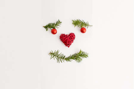 Happy face handmade with Christmas tree branches, red balls and red heart. Flat lay