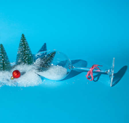 Snow and a Christmas tree fall out of a glass of wine on a blue background. Red decorative balls