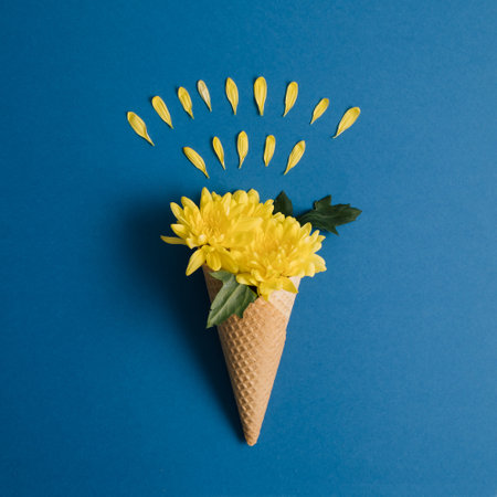 Yellow flowers and ice cream cone on blue background. Minimal concept. Flat lay.の写真素材