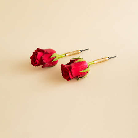 Creative arrangement with red flowers as darts on a beige background. Minimal nature or game...