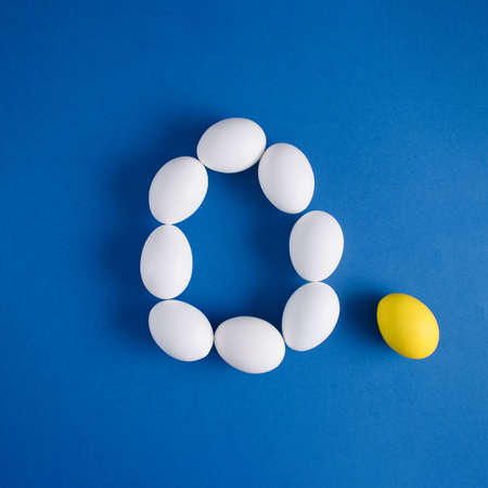 White and yellow eggs arranged in the shape of an Easter egg on a light blue background. Minimal Easter or food layout. Creative copy space. Holiday concept. Flat layの写真素材