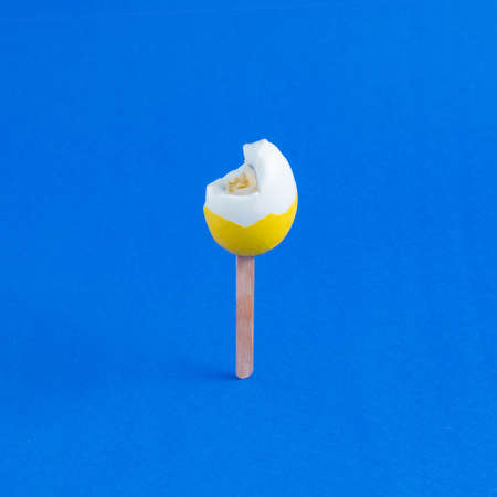 Yellow eggs bitten on a stick like ice cream on a blue background. Minimal creative concept of Easter or food.の写真素材