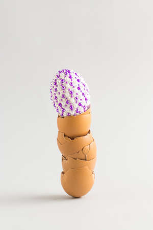 The creative Easter concept of natural eggs with purple stickers stands on a shell of broken eggs on a yellow background. Minimal holiday or food concept.の写真素材