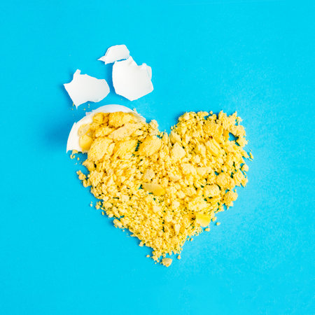 A creative Easter art concept with a heart made of natural egg yolk and an egg shell on a light blue background. Minimal holiday and food conceptの写真素材