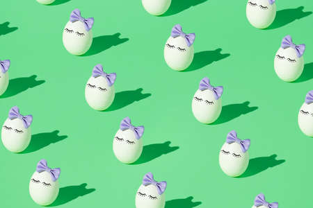 Pattern made of White Easter egg with eyelashes and purple bow tie headband on a light green...