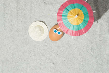 Creative Easter composition with egg, hat and beach umbrella on the sand. Summer and holiday idea....