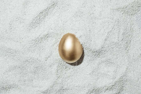 A creative Easter concept with a golden egg covered in sand on the beach. Summer and holiday idea....