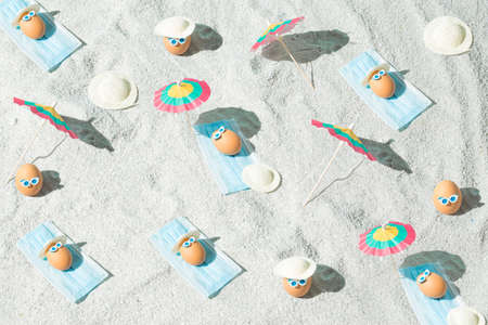 Summer Easter pattern background with eggs, virus mask, beach umbrella and glasses. Minimal pandemic or holiday concept. Safe distance. Top view.の写真素材