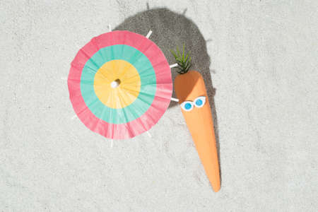 Creative Easter composition with carrots, glasses and beach umbrella on the sand. Summer and holiday idea. Flat lay.の写真素材