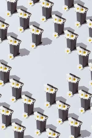 A creative nature pattern with white flowers growing from a trash can against a gray background....