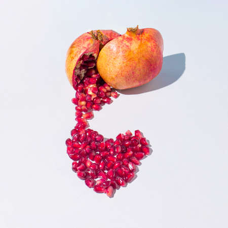 Creative composition with a freshly cut pomegranate makes a red heart on a gray background. Minimal fresh nature or love concept.の写真素材