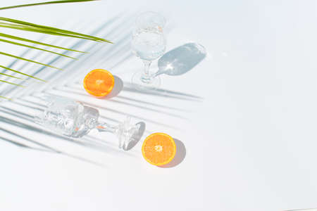 Creative summer composition with a fresh slice of orange, glasses and a palm branch on a blue and gray background. Cold drink or refreshment concept.の写真素材