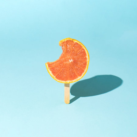 Creative Summer idea with red grapefruit and ice cream stick on a light blue background. Organic tropical fruit juice. Minimal summer food.の写真素材