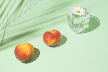 Creative summer composition with fresh peach fruits, a glass of drink and flowers against a pastel...
