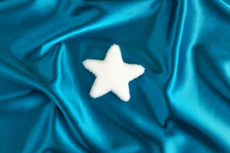 White Christmas star on luxurious blue satin. Elegant decorative holiday background. Creative Xmas or New year festive holiday concept.の写真素材