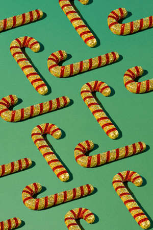 Trendy pattern with red Christmas candy canes on a light green background. New Year holiday...