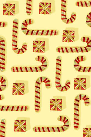 Trendy pattern with red Christmas candy canes and gift boxes on a yellow background. New Year...