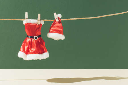 Creative Christmas layout with a clean red Santa Claus suit and hat dries on a rope against a green background. Minimal Xmas or New Year celebration concept.の写真素材