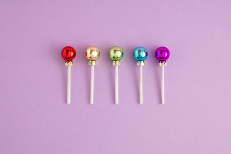 Creative concept with colorful Christmas baubles like a lollipops on a purple background. Minimal...