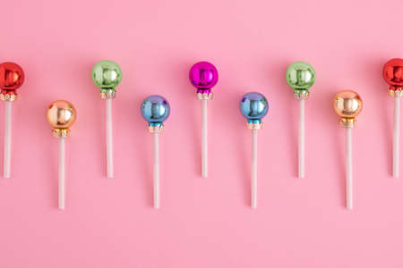 Creative concept with Christmas baubles like a lollipops on a pastel pink background. Minimal New year candy conceptの写真素材