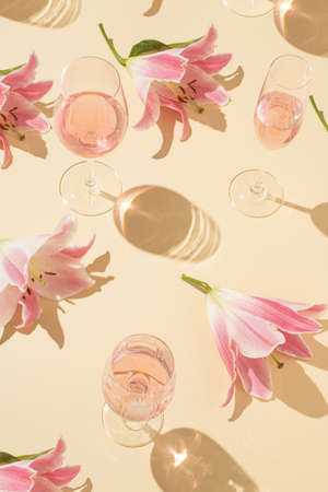 Champagne and wine glasses with pink flowers on a beige background. Minimal Valentine's Day or Woman's day layout. Natural party background.の写真素材