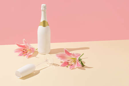 Champagne bottle and glass with pink flowers on a beige background. Minimal Valentine's Day or Woman's day layout. Nature party sceneの写真素材