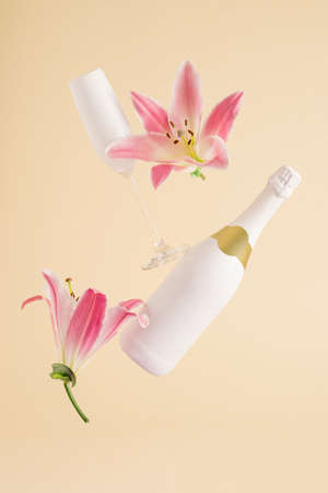 Champagne bottle and glass with pink flowers levitate on beige background. Minimal Valentine's Day or Woman's day layout. Nature party conceptの写真素材