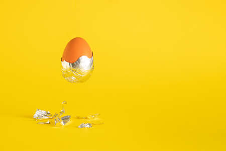 Creative Easter egg with foil against an yellow background. Creative holiday or futuristic concept.