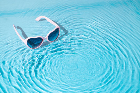 Trendy sunny scene with heart-shaped sunglasses in the water. Summer travel concept. Minimal love...
