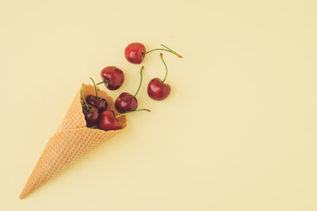 Trendy summer composition with fresh red cherries and ice cream cone on pastel yellow background. Minimal summer food idea.の写真素材