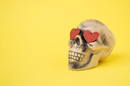 Skull with red hearts against a yellow background. Halloween love and romantic concept.の写真素材