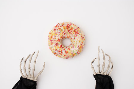 Minimal Halloween concept with skeleton hands and sweet colorful donuts on a white background. Party or food concept.の写真素材