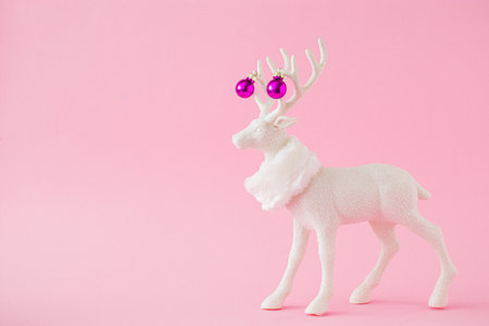 White reindeer with scarf and pink Christmas baubles against a pastel pink background. Minimal New Year or Christmas concept.の写真素材