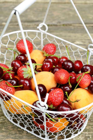 Wire basket full of summer fruits and berries - peaches, apricots, strawberry and sweet cherry on...
