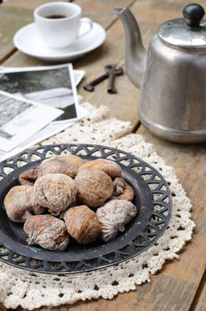 Still life with dried figs on lace doily, coffee pot, cup of coffee and vintage cards on wooden backgroundの写真素材