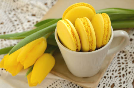 Cup with yellow French macarons and yellow tulips on old book