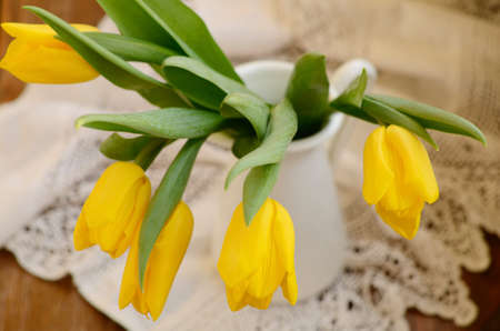 Yellow tulips in white jug on vintage lace doily