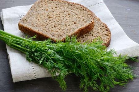 Dark bread and bunch of fresh dill on linen table napkinの写真素材