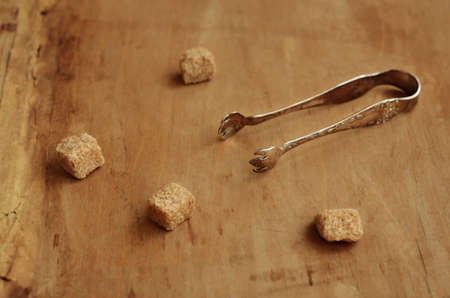 Vintage silver plated sugar tongs and pieces of cane sugar over aged brown backgroundの写真素材